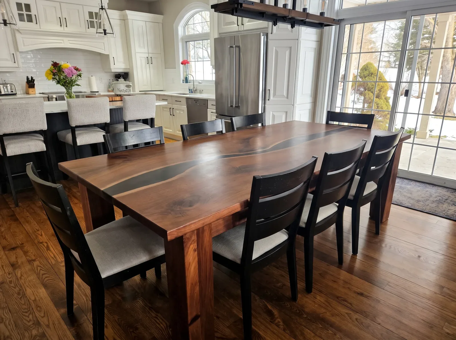 Black walnut dining table with a poured epoxy river, seating eight, installed in a client's kitchen